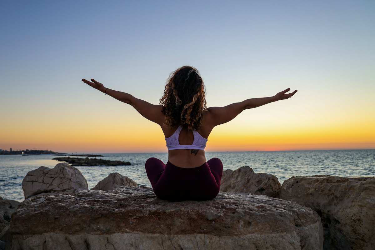 A woman standing at the shore at sunrise with her arms open
